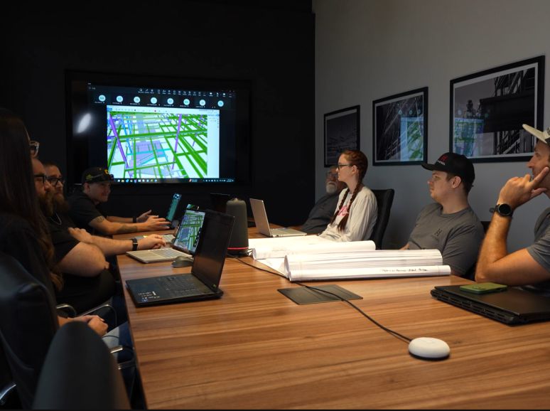Team meeting with laptops and drawings, a 3D steel model on the screen