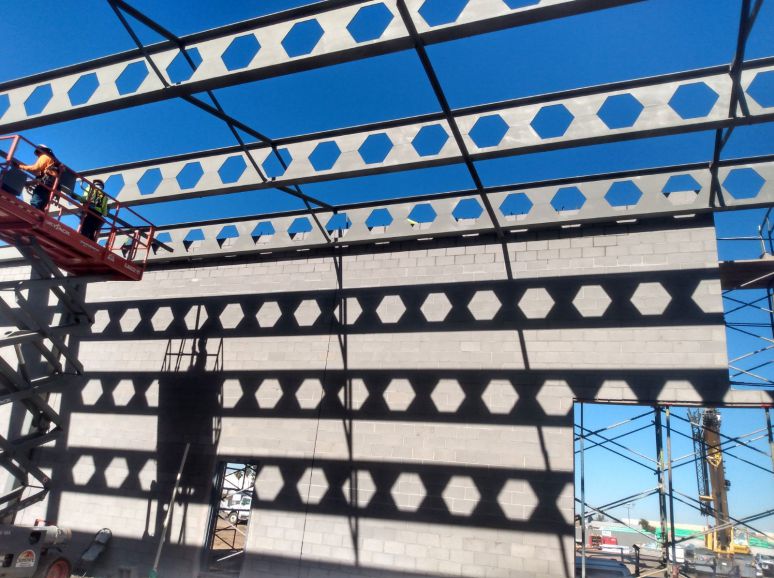 Steel frame with hexagonal-cut beams under a blue sky